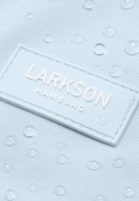 Világoskék anyag, amelyen kiemelkedő kör alakú cseppek találhatók, az alján pedig egy fehér téglalap alakú címke áll az "LARKSON HAMBURG" felirattal.