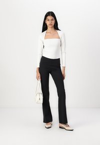 Valkoinen pitkähihainen paita neliömäisellä kauluksella, yhdistettynä mustiin slim fit -hoseihin ja beigeihin ballerinatossuihin. Malli pitää kädessään pientä valkoista laukkua.