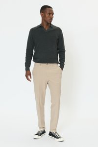 Ciemnoszary sweter z dzianiny z dekoltem w serek, beżowe dopasowane spodnie i czarne sneakersy z białymi podeszwami. Nowoczesny krój z luźną sylwetką.