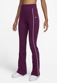 Pantalons de sport violets avec une taille haute, dotés de bandes blanches sur les côtés et de fentes aux ourlets. Le matériau semble doux et extensible. Logo Nike présent.