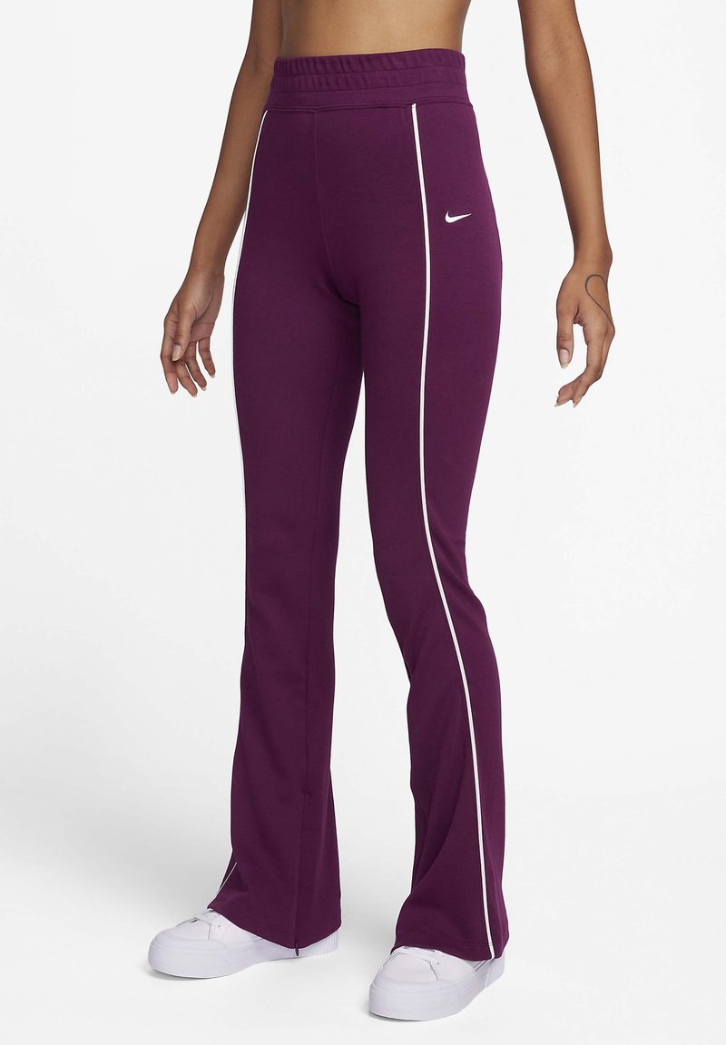 Pantalons de sport violets avec une taille haute, dotés de bandes blanches sur les côtés et de fentes aux ourlets. Le matériau semble doux et extensible. Logo Nike présent.