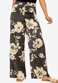 Black wide-leg pants with a cream floral pattern and polka dots. Smooth fabric, high waist, and side pockets. Minimalist design elements.