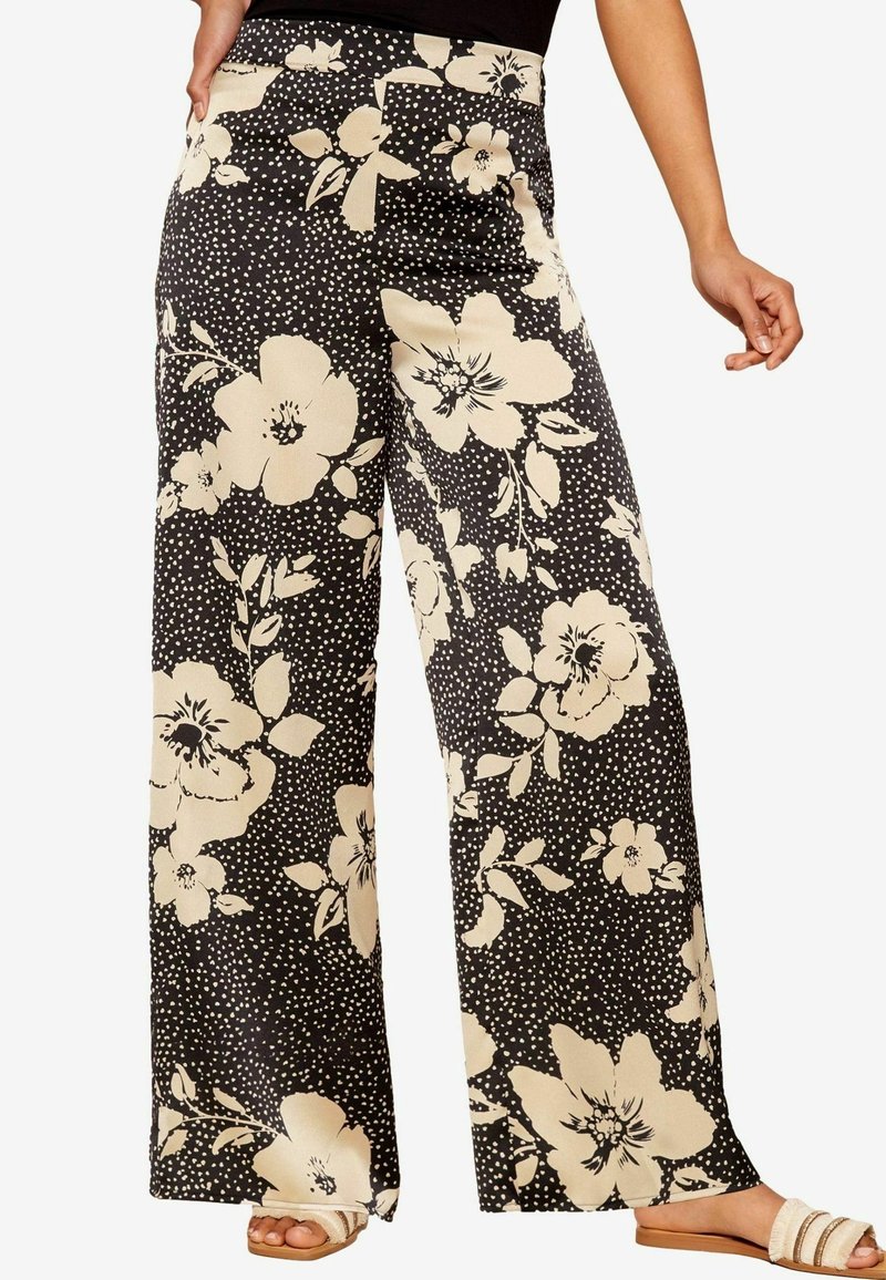Black wide-leg pants with a cream floral pattern and polka dots. Smooth fabric, high waist, and side pockets. Minimalist design elements.