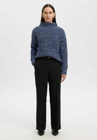 Maglione blu lavorato a maglia con colletto alto e vestibilità rilassata, abbinato a pantaloni neri a gamba dritta e scarpe nere a punta.