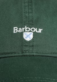 Grüne Baseballmütze aus Baumwolle, mit weißem gesticktem "Barbour"-Logo und einem blauen Schild mit einem "X"-Symbol auf der Vorderseite.