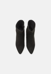 Botines negros hasta el tobillo con punta afilada y una textura de ante suave. Cuenta con un cierre de cremallera lateral y una silueta ajustada.