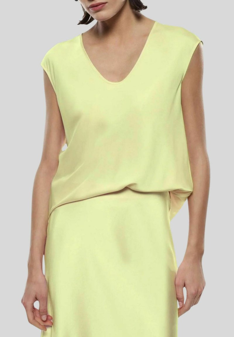 Top giallo senza maniche con scollatura a V, realizzato in tessuto liscio. Presenta una vestibilità ampia e una leggera drappeggiatura all'orlo.