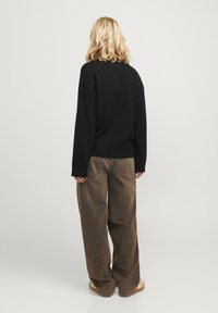 Svart, texturerad tröja med en lös passform, tillsammans med vida, bruna corduroybukser. Outfiten har en rund halsringning och långa ärmar.