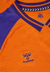 Orange tröja med lila accenter, med ett texturerat mönster. Inkluderar en svart och orange randig krage samt en logotyp i det nedre hörnet.