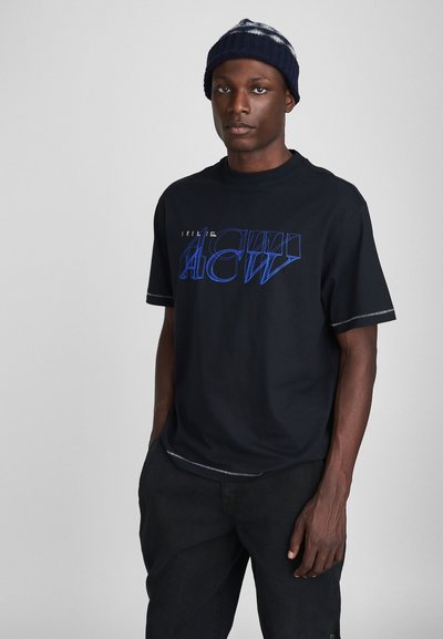 Sort kortærmet t-shirt med blå grafisk tekst. Casual pasform, rund halsudskæring, kontrasterende syningsdetalje, båret med mørke bukser og en blå strikket hue.