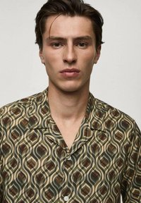 Kortærmet skjorte med et retro bladmønster i grøn, brun og creme. Fremstillet af letvægtsstof med en klipkrave og knaplukning.