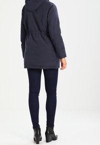 Námořnická péřová bunda s kapucí, elastickým pasem, dlouhými rukávy a postranními kapsami. Nosit s tmavými slim kalhotami a černými kotníkovými botami na podpatku.