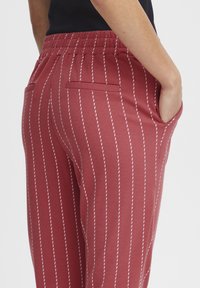 Pantaloni a righe rosse realizzati in un tessuto morbido, con un elastico in vita e tasche laterali con dettagli di cucitura bianca.