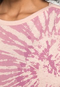 Lichtroze T-shirt met een tie-dye patroon in verschillende tinten roze. Zacht materiaal en een brede halslijn. Het ontwerp bevat stervormige figuren.