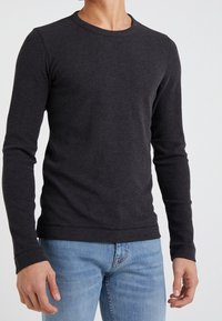 Long-sleeve, crew-neck shirt in dark gray, made from a textured fabric. Fitted design, paired with light blue jeans, showcasing a casual style.