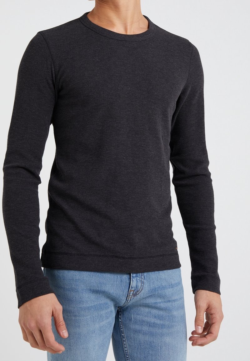 Long-sleeve, crew-neck shirt in dark gray, made from a textured fabric. Fitted design, paired with light blue jeans, showcasing a casual style.