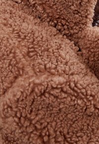 Brun, fluffig tyg med en mjuk, texturerad yta, med en kramig, skrynklig utseende och ojämn, plyschliknande högar.