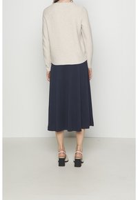Beige ribbad sweater med rund halsringning, parat med en marinblå A-linje klänning. Outfiten kompletteras av vita blockklack sandaler.