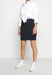 Námořnická bavlněná sukně s přiléhavým střihem, spárovaná s bílou košilí na knoflíky uvázanou v pase a bílými teniskami s růžovými akcenty.