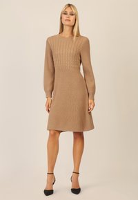 Strickkleid in einem hellbraunen Farbton mit einem strukturierten Zopfmuster im Oberteil, langen Ärmeln und einem schwingenden Rock, der knapp über dem Knie endet.
