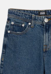 Κοντινή λήψη μπλε τζιν παντελονιού που δείχνει τις μπροστινές τσέπες, ασημένιους κρίκους, κουμπί με ραφή και μαύρη ταμπέλα με την επωνυμία Jack & Jones.