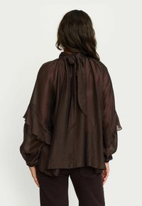 Blouse transparente marron foncé avec des manches volantes et un col noué. Tissu léger avec une silhouette fluide, un design en couches et une finition texturée.