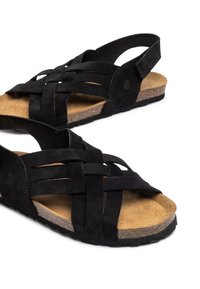 Sandales en daim noir avec un design supérieur tissé et un dos ouvert. Semelle en liège et semelle extérieure en caoutchouc texturé pour une meilleure accroche.