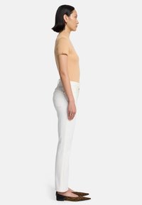Beige gebreide top met korte mouwen, hoge hals; witte rechte jeans; puntige zwarte en bruine panterprint ballerina's.