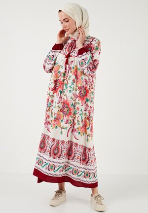 Floral-patterned long dress in white with red and green accents; features a high neck, long sleeves, and a flowing skirt. Worn with a beige hijab.