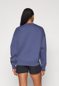 Marinblå oversized sweatshirt med rundad halsringning och ribbad fåll, framhävd över svarta shorts. Mjuk tygkvalitet och avslappnad passform.