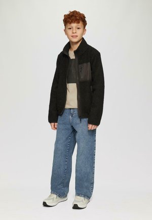 Zwarte fleecejack met textuurstof en een zwart ritssluiting borstzak. Gecombineerd met lichtblauwe jeans en witte sneakers.