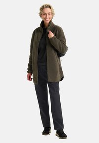 Fleecejacke in dunkelolivgrün mit Reißverschluss, kombiniert mit einem schwarzen Oberteil und dunklen Hosen, ausgestattet mit einer lockeren Passform und weichem Stoff.