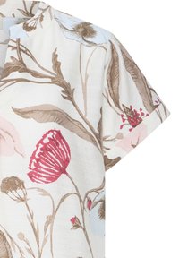 Chemise blanche à manches courtes avec des motifs floraux beige, rouge et bleu comprenant de grandes feuilles et des fleurs épanouies.