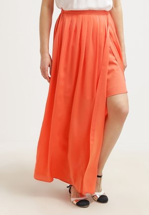 Kvinde iført en orange plisseret wrap-nederdel med indre shorts, kombineret med hvide og sorte sko med ankelrem.