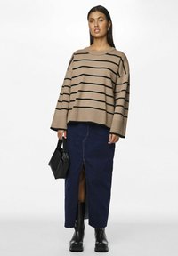 Pull en grosse maille beige à rayures noires, associé à une jupe en denim foncé avec une fente avant, et des bottines noires.
