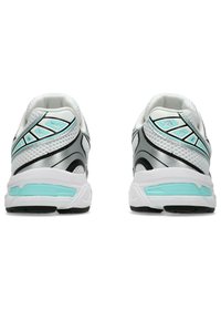 Baskets de sport blanches avec des accents argentés et des détails en turquoise. Elles présentent un dessus en mesh, une semelle rembourrée et des lignes courbes distinctives sur les côtés.