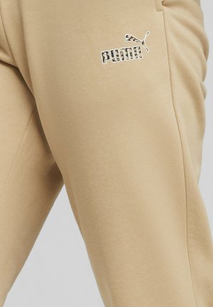 Pantaloni della tuta beige realizzati in tessuto morbido, con il logo e l'emblema Puma bianchi. Il design include tasche laterali e una vestibilità comoda.
