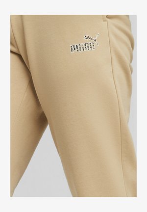 Pantaloni della tuta beige realizzati in tessuto morbido, con il logo e l'emblema Puma bianchi. Il design include tasche laterali e una vestibilità comoda.