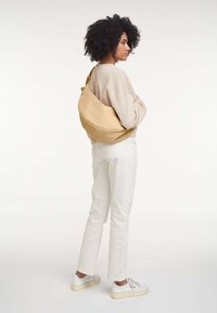 Borse a tracolla beige con una forma morbida, realizzata in materiale morbido, caratterizzata da una forma curva, cuciture minime e una singola tracolla regolabile.