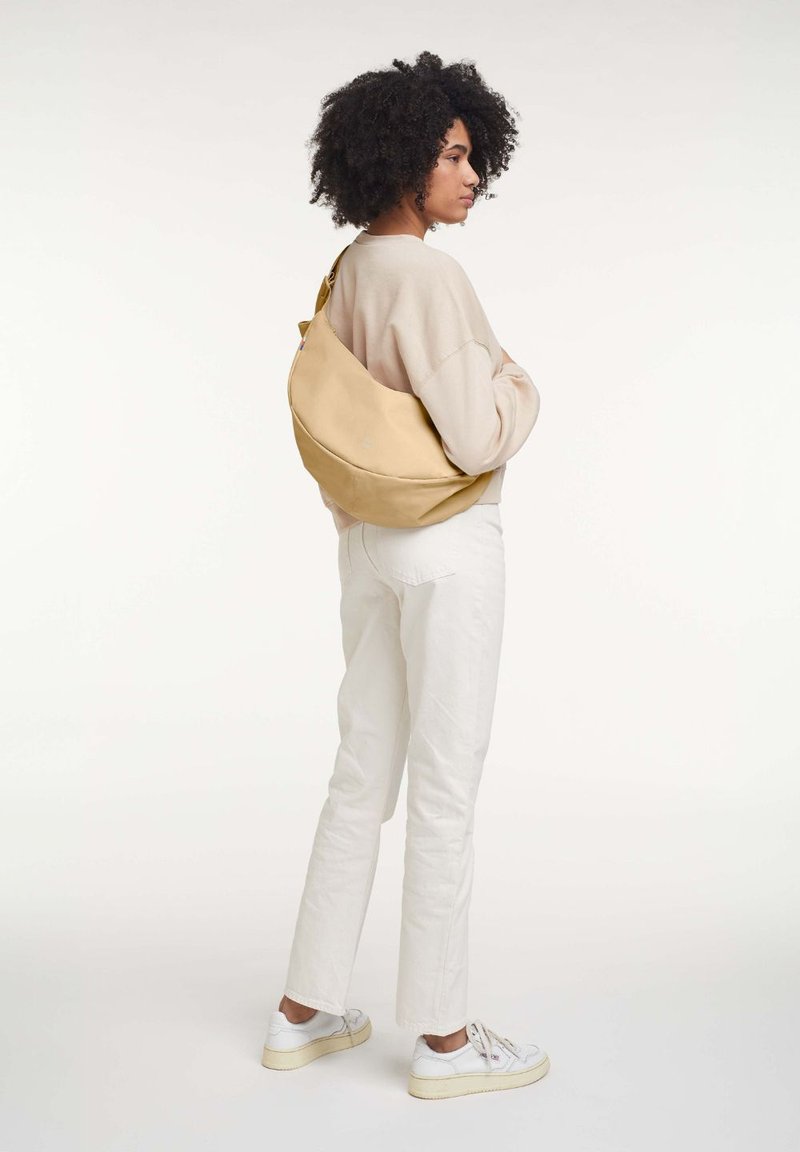 Beige slouchy handväska gjord av mjukt material, med en kurvig form, minimala sömmar och ett justerbart axelband.