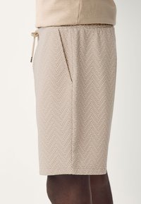 Bézs mintás rövidnadrág halszálkamintás textúrával, elasztikus derékrésszel, húzózsinóros záródással és oldalzsebekkel.