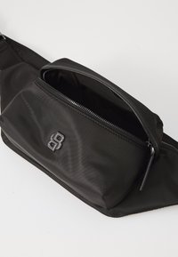 Crni najlon hip ruksak s glavnim odjeljkom na rajsferšlus, elegantnim dizajnom i teksturiranom površinom. Ima crni logo sa prednje strane.