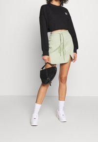 Sudadera negra corta, falda mini verde claro con cordón, y bolso negro texturizado. Zapatillas blancas con calcetines hasta el tobillo completan el look.
