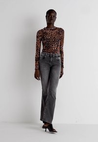 Tijgerprint lange mouw top gecombineerd met hoge taille, rechte grijze spijkerbroeken. Model draagt zwarte open teen hakken. Eenvoudige witte achtergrond.