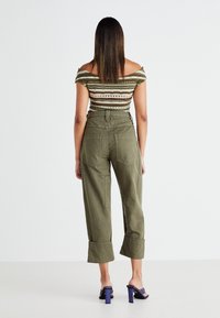 Pantalones cargo verde olivo de corte relajado, con tobillos ajustados y bolsillos traseros. Combinados con una blusa de hombros descubiertos de estampado y sandalias de tacón moradas.