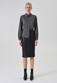 Camicia a maniche lunghe con bottoni a righe verticali bianche e nere, abbinata a una gonna in pelle nera aderente e stivaletti con dettagli decorativi.