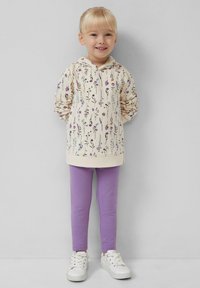 Jasnobeżowa bluza z kapturem w kwiatowy wzór, fioletowe legginsy i białe sneakersy. Miękki materiał, luźny krój, długie rękawy i kaptur.