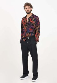 Pantaloni jogging neri con cintura regolabile abbinati a una camicia con bottoni a fantasia multicolore che presenta onde e disegni intricati.