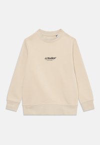 Bež dugih rukava pulover s crewneck izrezom s logotipom "JJ Studios" ispisanim crnom bojom u središtu prsnog dijela.