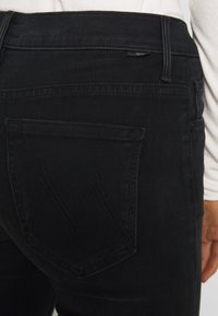 Svarta denimjeans har en platt bakficka med ett utmärkande chevronstickmönster. Tyget har en slät, mjuk textur.